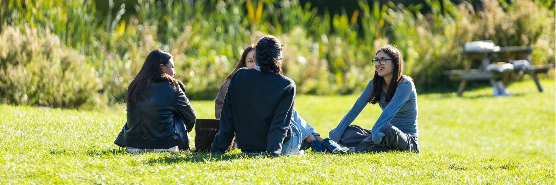 Three students sitting next to lake on bath campus
