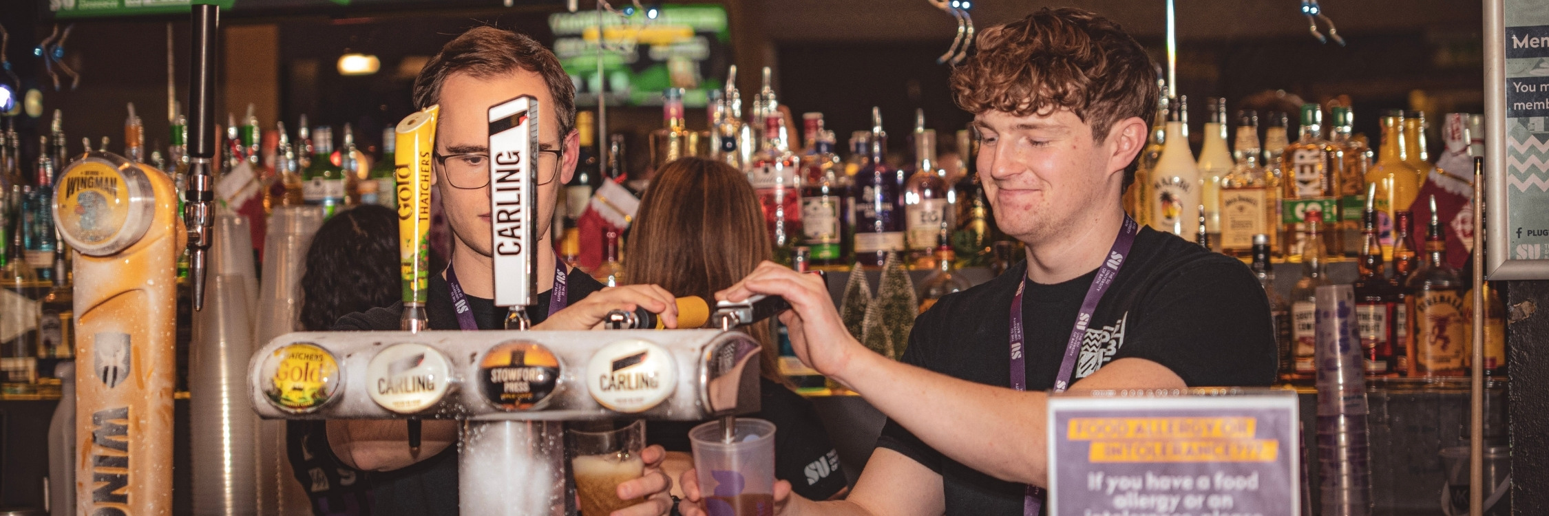 Two guys pouring pints behind student bar