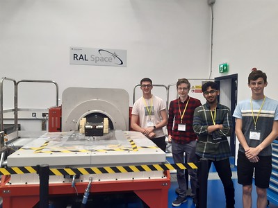 Four members of TBRo standing next to the vibration table with their rover on top of the disc.