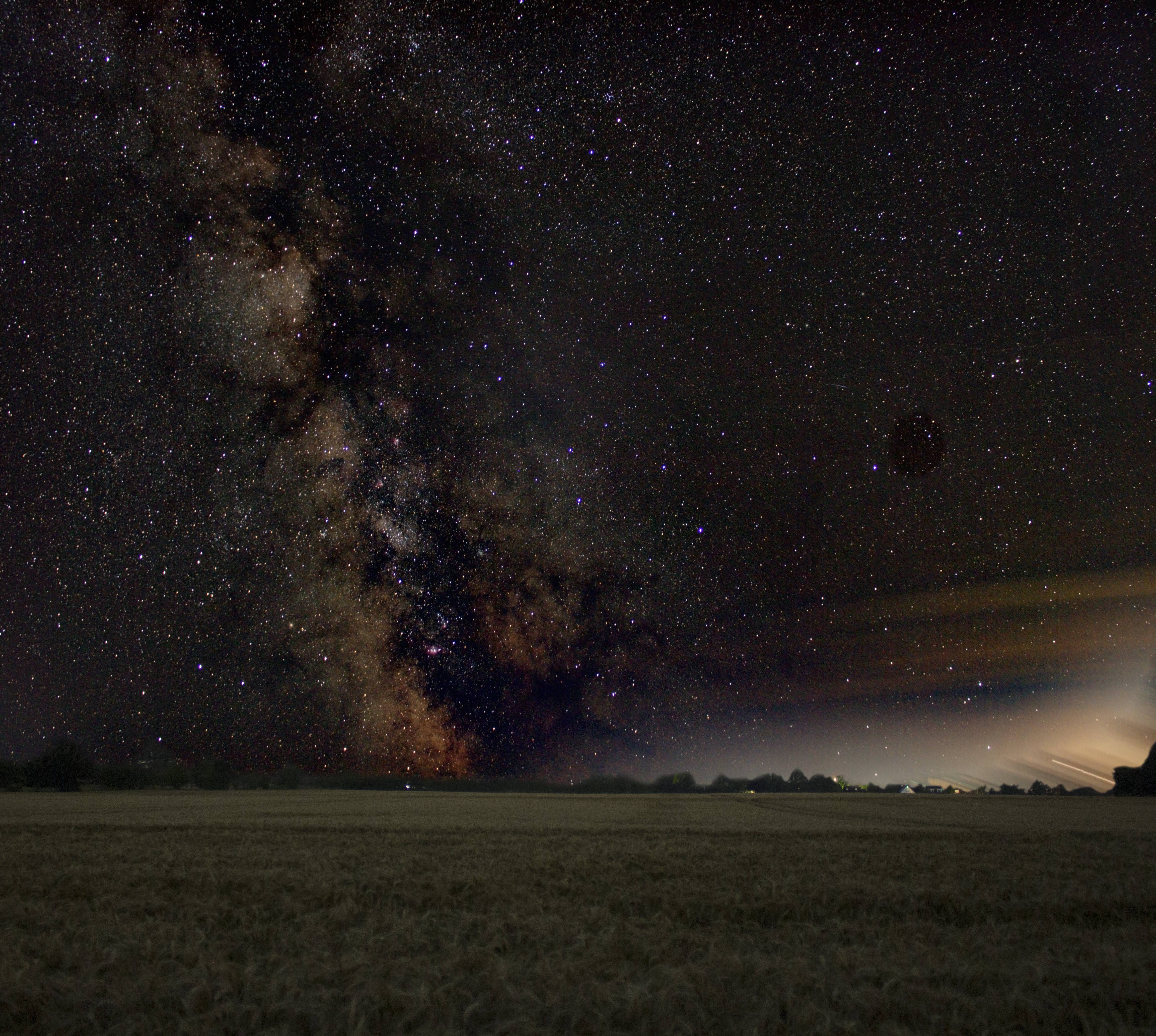 Composite image of the milky way above a grassy field.