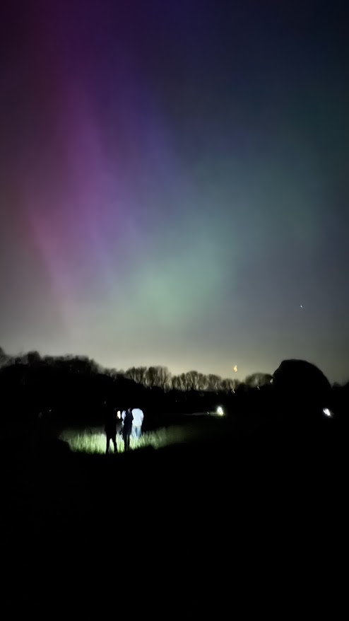 Two students lit up by a torch underneath a colourful aurora