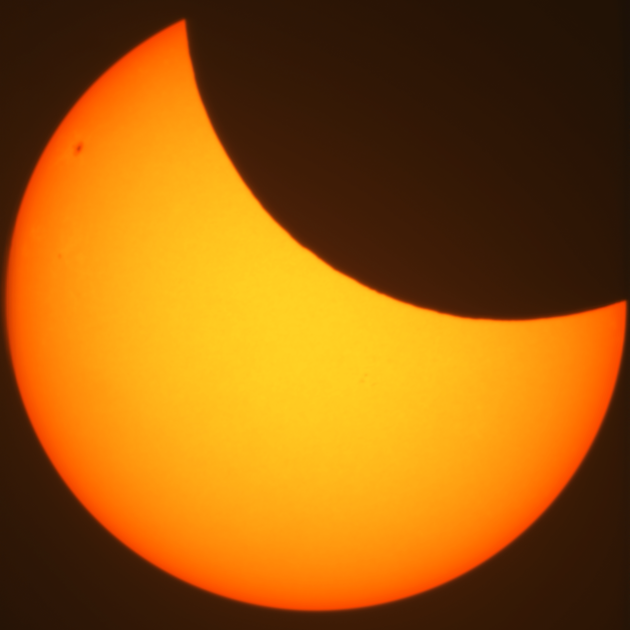 Centered colour photo of the sun during a partial eclipse. Some sunspots are visible.