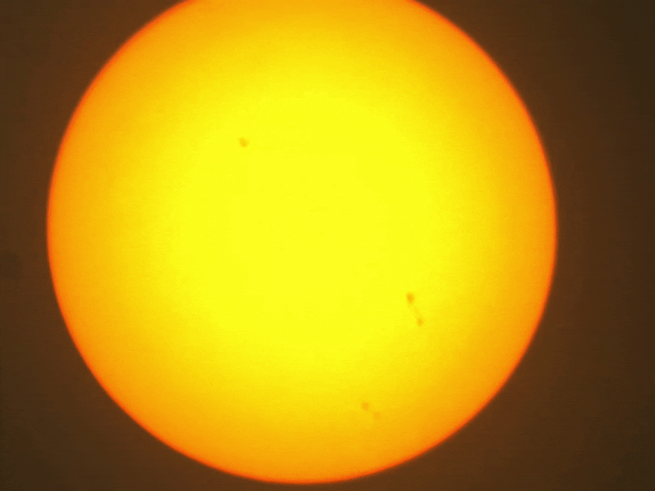 Wobberly colour video of the sun. Some sunspots are visible. A blurry ISS travels from right to left.